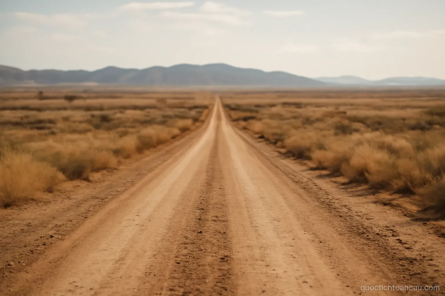 a long dirt road crossing dry open land with low hills far in the distance