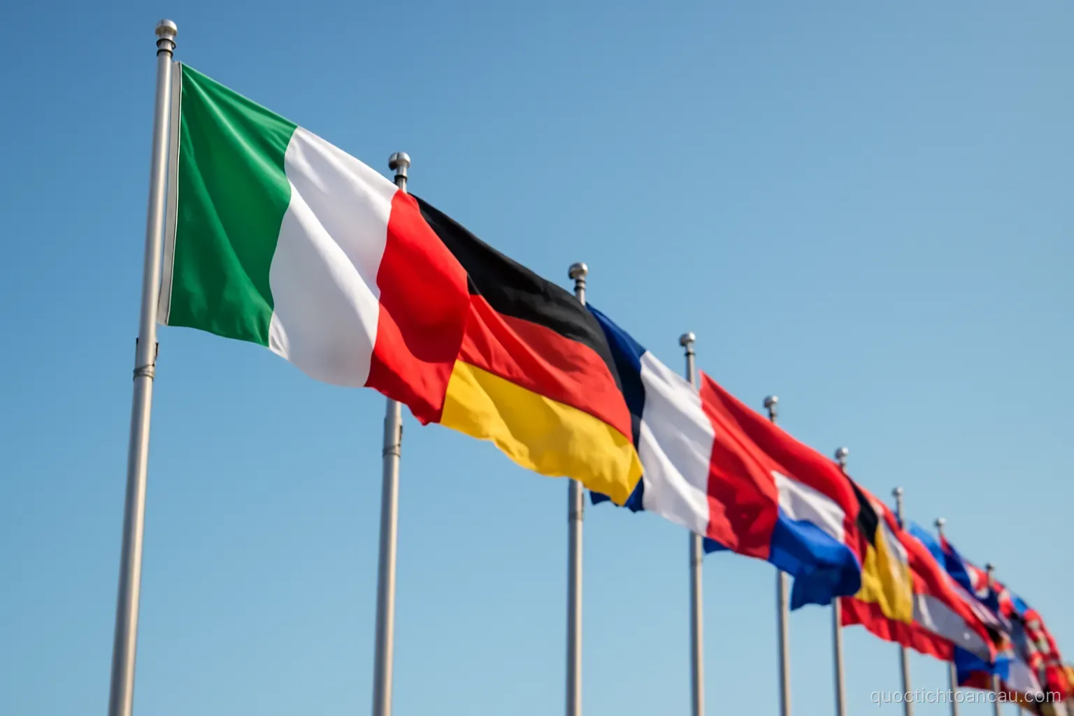 a row of national flags on poles seen from below against a clear sky